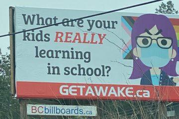 Billboard with a the caricature of a purple haired school teaching with glasses and angry eyebrows wearing a medical mask superimposed over a Progress Pride flag showing the white pink and blue colors representing transgender people. The words "What are your kids REALLY learning in school" are written on the billboard.