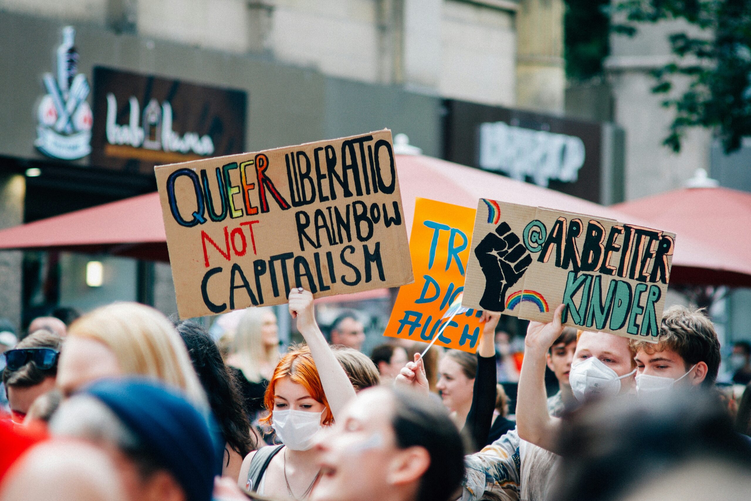 Pride 2024: A Clarion Call for Activism. Image of a Pride march with a sign that says Queer Rights not Rainbow Capitalism