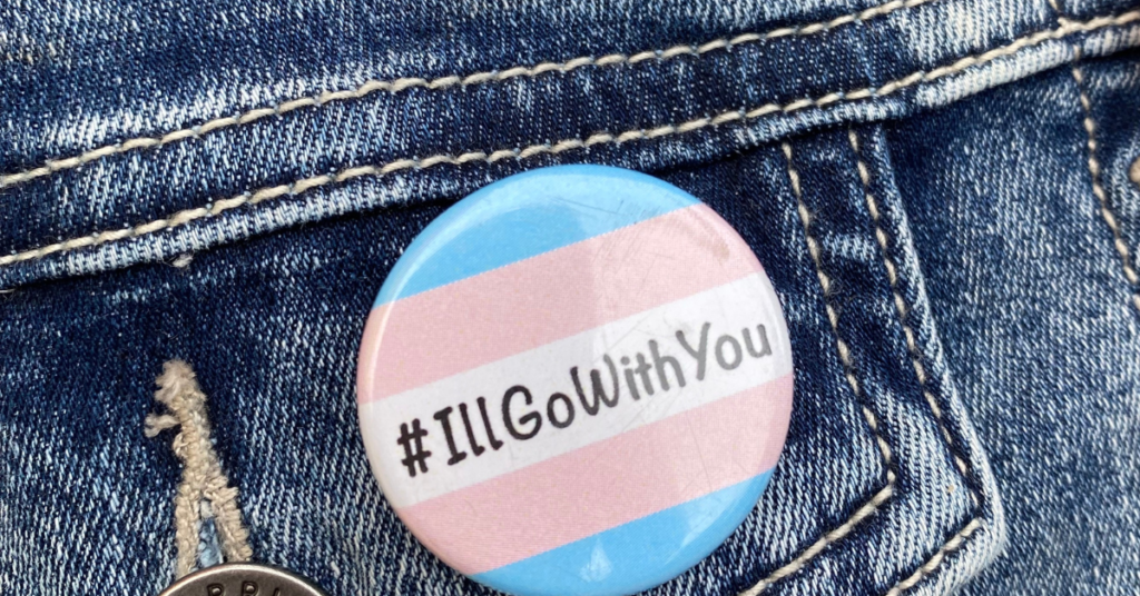 How to be a trans ally button in trans flag colours with #Illgowithyou pinned to a blue jean jacket